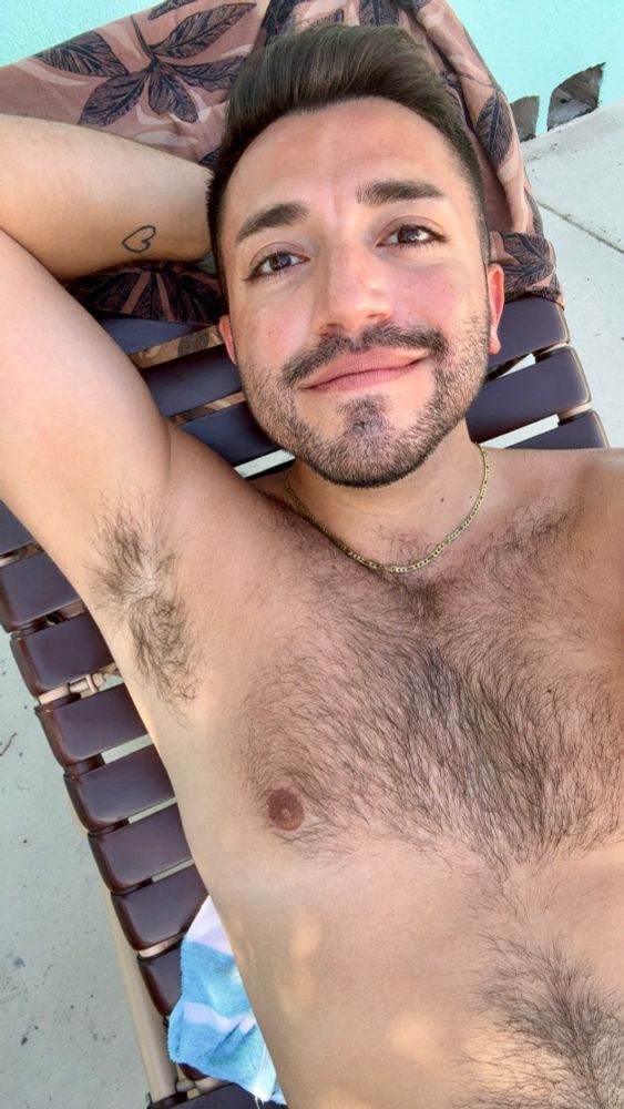 selfie of me at the pool laying down on a pool chair with my arm behind my head, shirtless wearing a gold chair 