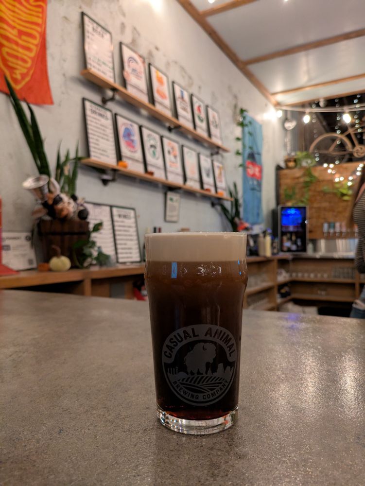 A glass of stout settling on a concrete bar. A tap wall with flags in the background