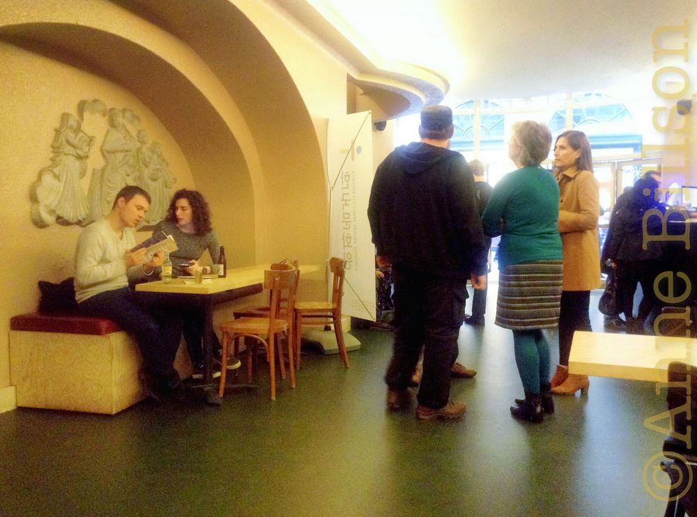 The foyer at Cinema Galeries in Brussels. On the left, a couple sits beneath an arched alcove. On the right, four people stand around and talk. The lighting is rather nice.