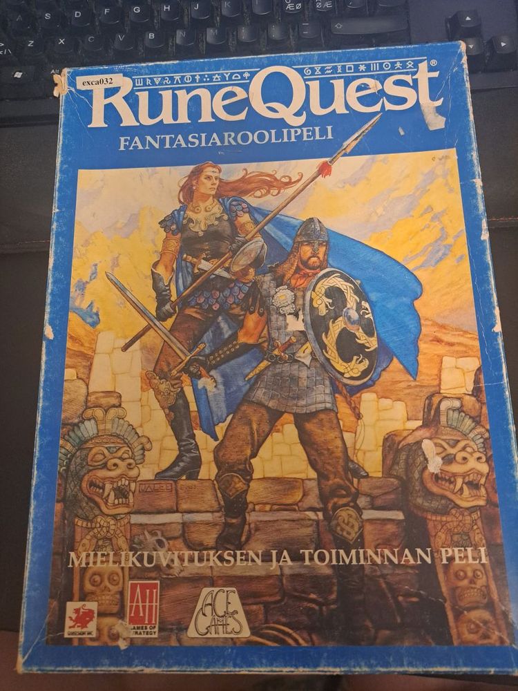 A boxed set of RuneQuest 3e TTRPG, translated to Finnish. It's a blue box with a cover art showing two human adventurers, a blue-cloaked spearwoman and a swordsman, standing on vaguely Meso-American looking temple steps.