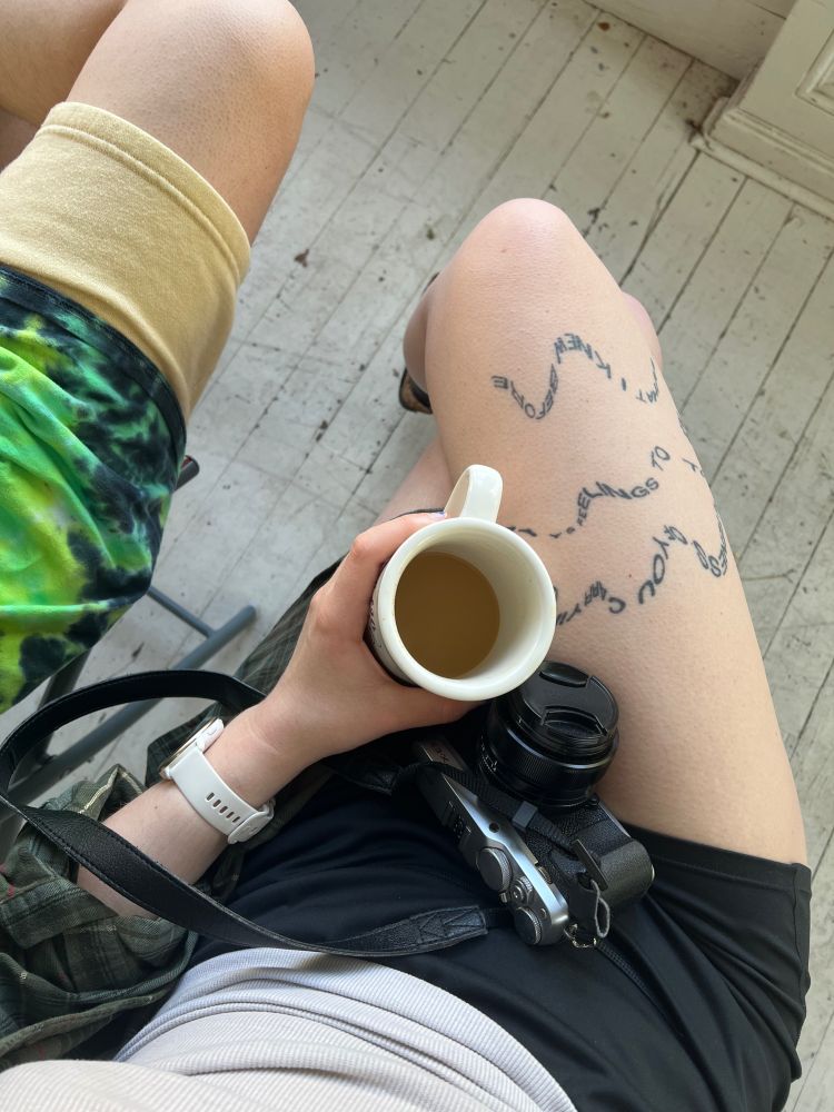 overhead photo of two people’s legs etc sitting in a very dirty porch; han’s holding a coffee cup and has a camera in their lap.