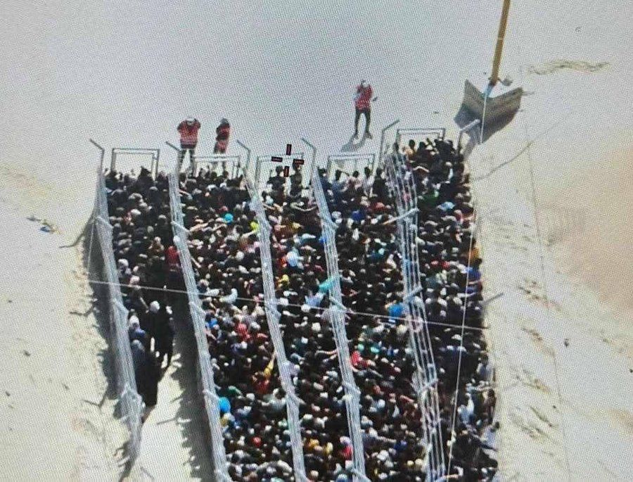 A large number of Palestinians are hemmed in to a crowded caged queuing system under the watch of US or Israeli guards, desperate to receive food