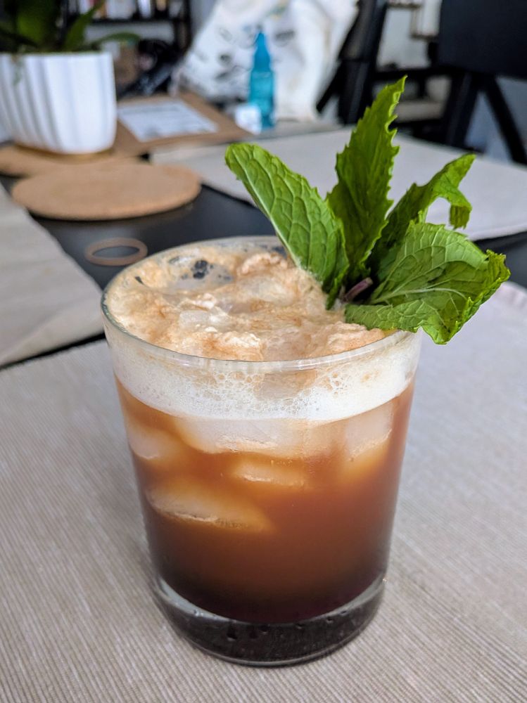 An espresso tonic with mint garnish sitting on a placement on a kitchen table