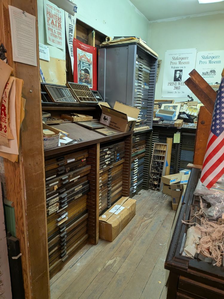 One side of the print shop at History Park San Jose, showing shelves of cases of wooden type among boxes and printed ephemera 