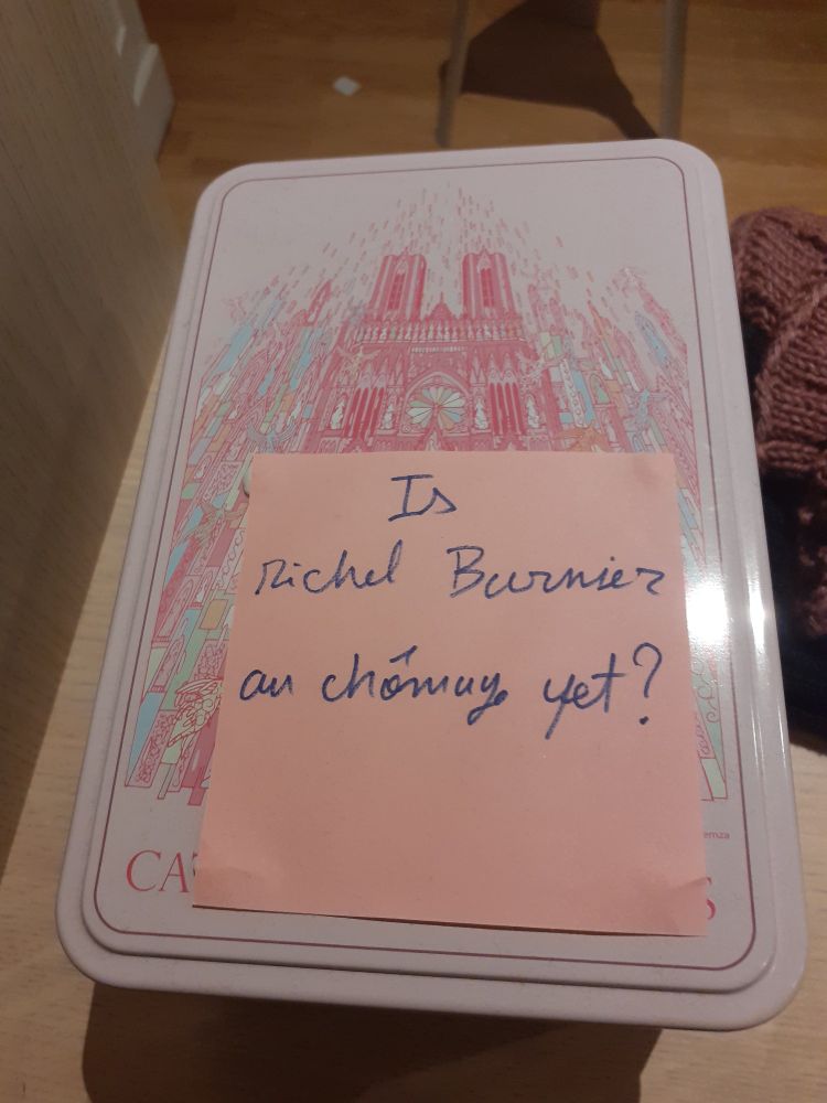Une boîre rose décorée d'une cathédrale, avec dessus un post it rose sur lequel est écrit au feutre bleu : "Is Michel Barnier au chômage yet ?"