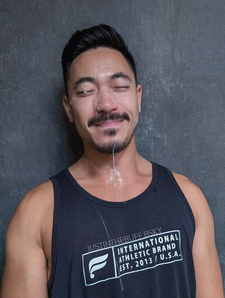 Justinthebuff laying back with his eyes closed while wearing a tank top while a white substance was shot all over his face as it drips down his face, lips, chin, and shirt. We may never know what this substance is but it sure looks like c*m