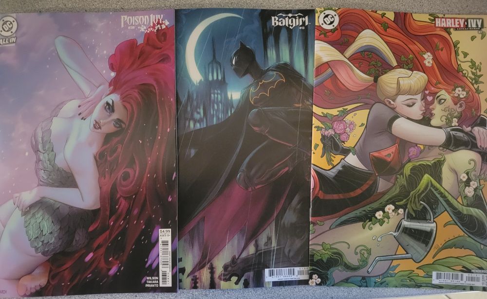 3 comics on a counter. Left to right: Poison Ivy #38 (Noobovich variant cover), Batgirl #13 (Malavia variant cover), and Harley & Ivy #1 (Torque & Rich variant cover)