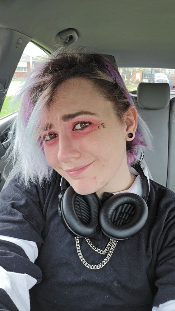 selfie of alt person with red eyeshadow black eyeliner, black moon stamps, and purple hair