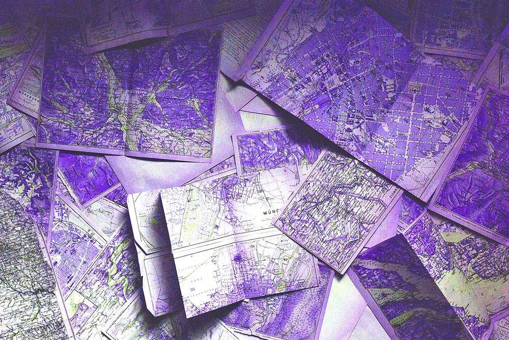 Photo of several maps, overlapping. The photo is manipulated so that the colours are violet and lime green.