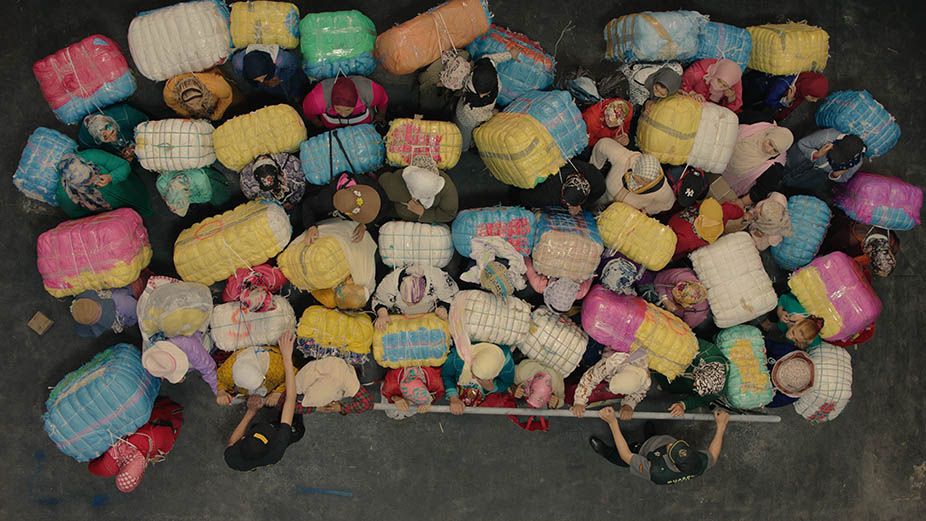 An overhead photograph of several persons carrying big bags, pressing against each other.