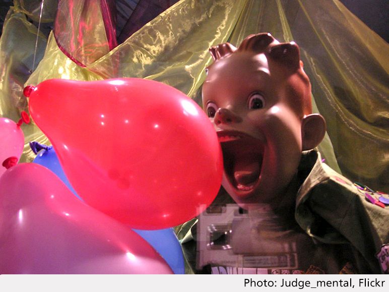Foto på en plastdocka som ler stort mot en röd ballong.