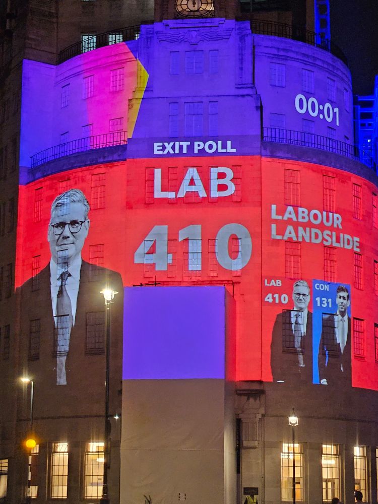 Shot of BBC Broadcasting House, with the words: 'Exit Poll - Lab 410 - Labour Landslide' projected onto it