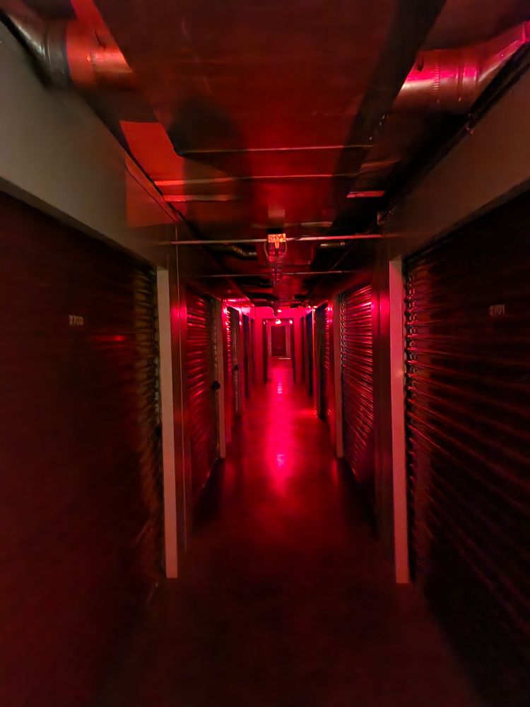 A picture showing a hallway glowing red - it's an interior storage unit building at night, illuminated by an exit sign at the end of the hallway. The camera picked up on more light than I could see.