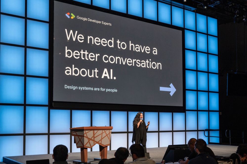 Me on stage in front of slide that says “we need to have a better conversation about AI”