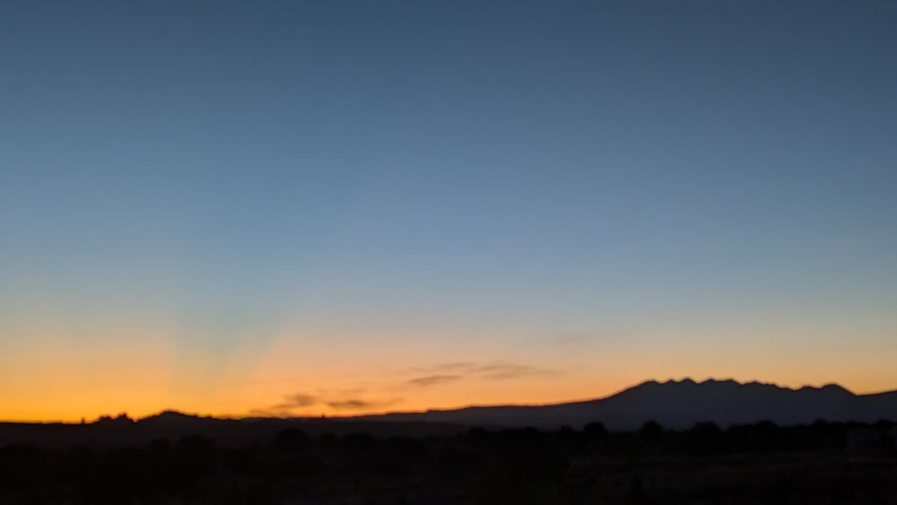 Taken before the sun rises, a dark landscape is bordered by orange. The top sky is still dark blue as night is being pushed away by the rising sun.