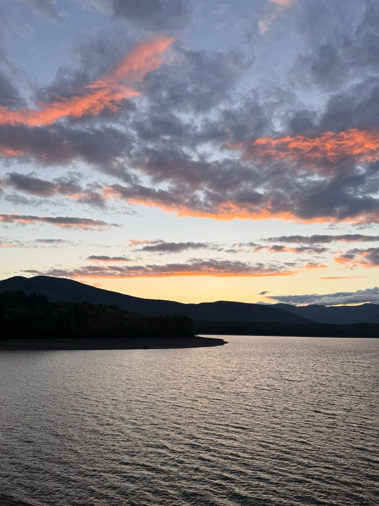 Sun has set behind mountains and a lake. There are clouds with bright pink at the edges.