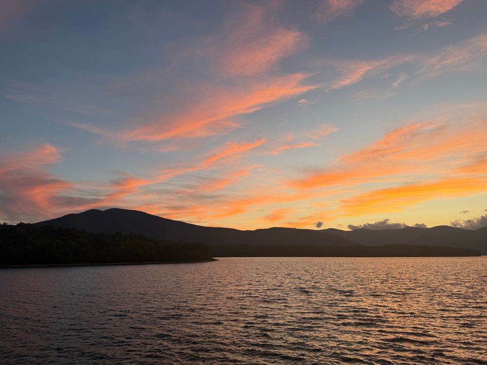 Just after sunset over mountains and a lake. There are glowing pink clouds.