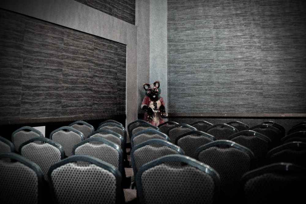 a pink sprinkledog, staring at you from the far side of the room at a corner, across a grid of chairs
