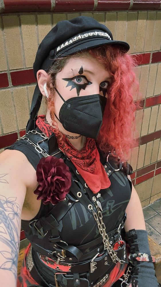 lilith (goth trans woman with red hair) wearing a cool hat sitting on a subway bench