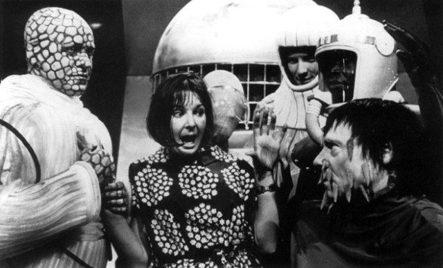 Verity Lambert surrounded by some of the alien delegates on what was her final episode as Doctor Who producer. The episode is called Mission to the Unknown (1965) she is wearing a dress and making a bit of a funny face to pretend she's frightened or something along those lines