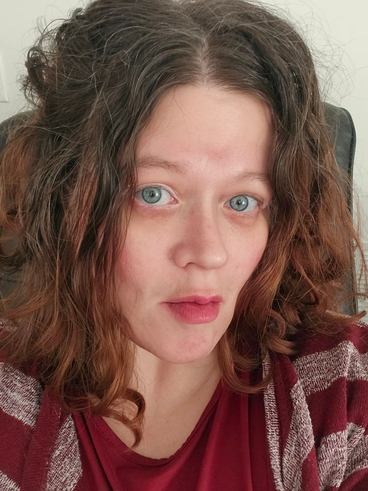 A color photo a selfie of a Caucasian woman with red hair and blue eyes wearing some makeup but not much it's me December 2025 I am also wearing a red dress and red stripe cardigan 