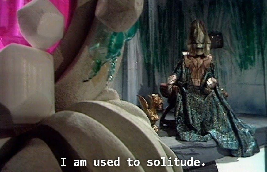Its Omega from Time Lord lore he is inside a very messy interior that is pink and green and sitting on his or her throne and states "I am used to Solitude" it is from a Doctor Who Episode called the three Doctors or the 3 Doctors 