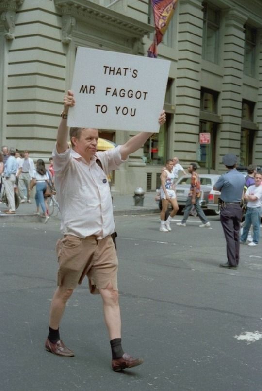 A man out in the street holding a sign that says "That's Mr Faggot to you" pride June 1990 new york