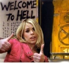 Rose Tyler in the Impossible Planet Doctor Who she is wearing a pink jacket and giving 2 thumbs up and behind her on the wall is spray painted "Welcome to Hell" along with a language that cant be translated