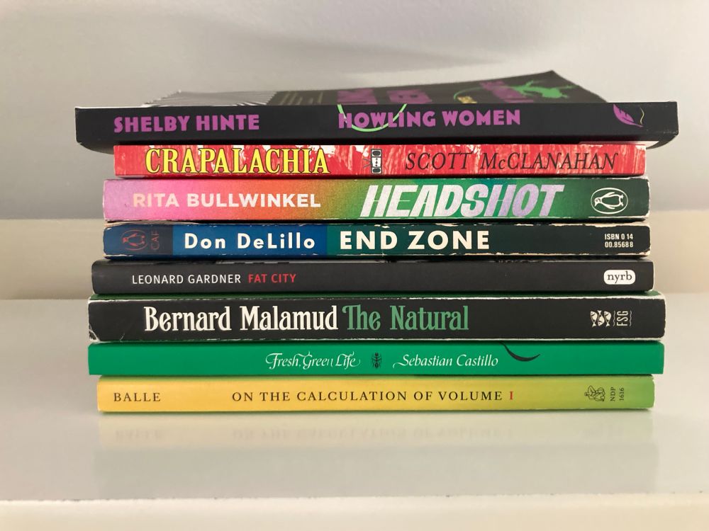 Photo of a stack of 7 paperbacks:

Howling Women, Shelby 
Crapalachia, Scott McClanahan
Headshot, Rita Bullwinkel
End Zone, Don DeLillo
Fat City, Leonard Gardner
The Natural, Bernard Malamud
Fresh, Green Life, Sebastian Castillo
On the Calculation of Volume I, Solvej Balle