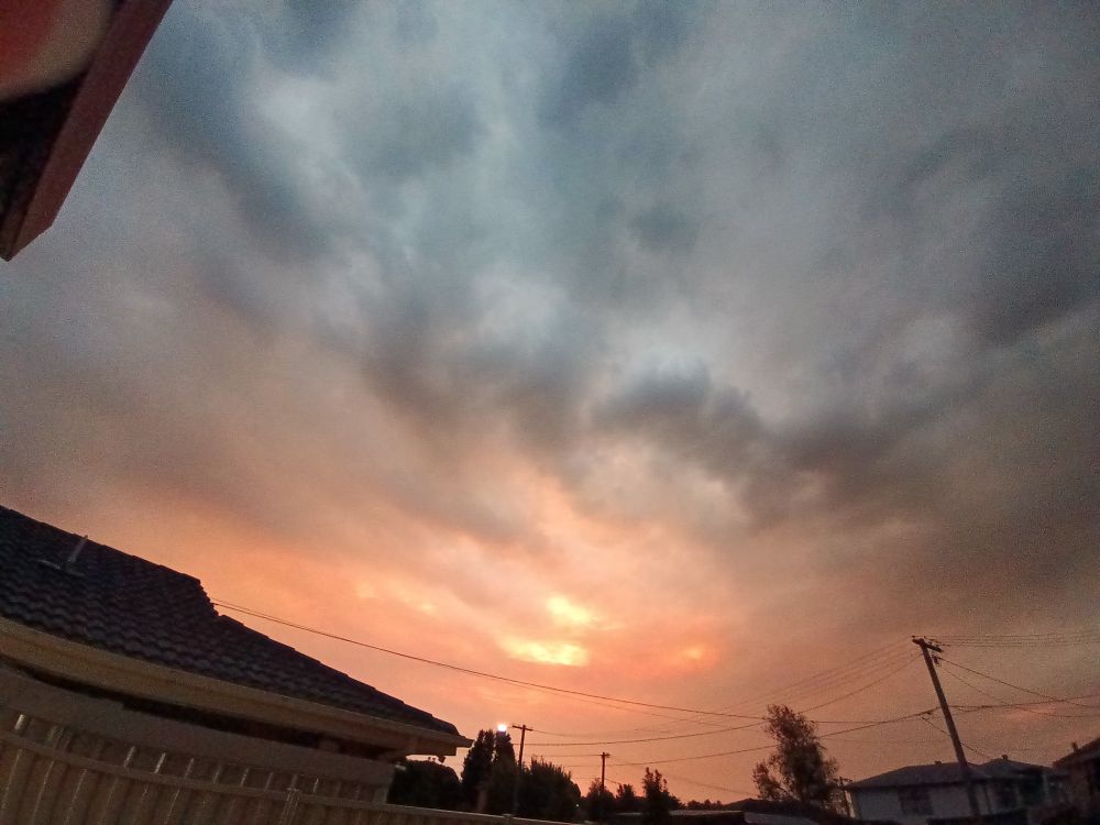 Orangey sunset through grey clouds and tops of houses