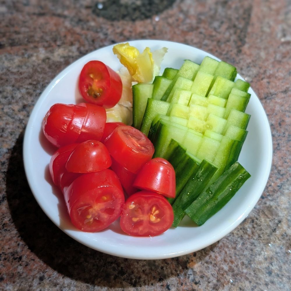 Tomatoes, lettuce bases, and cucumber on a small white dish 