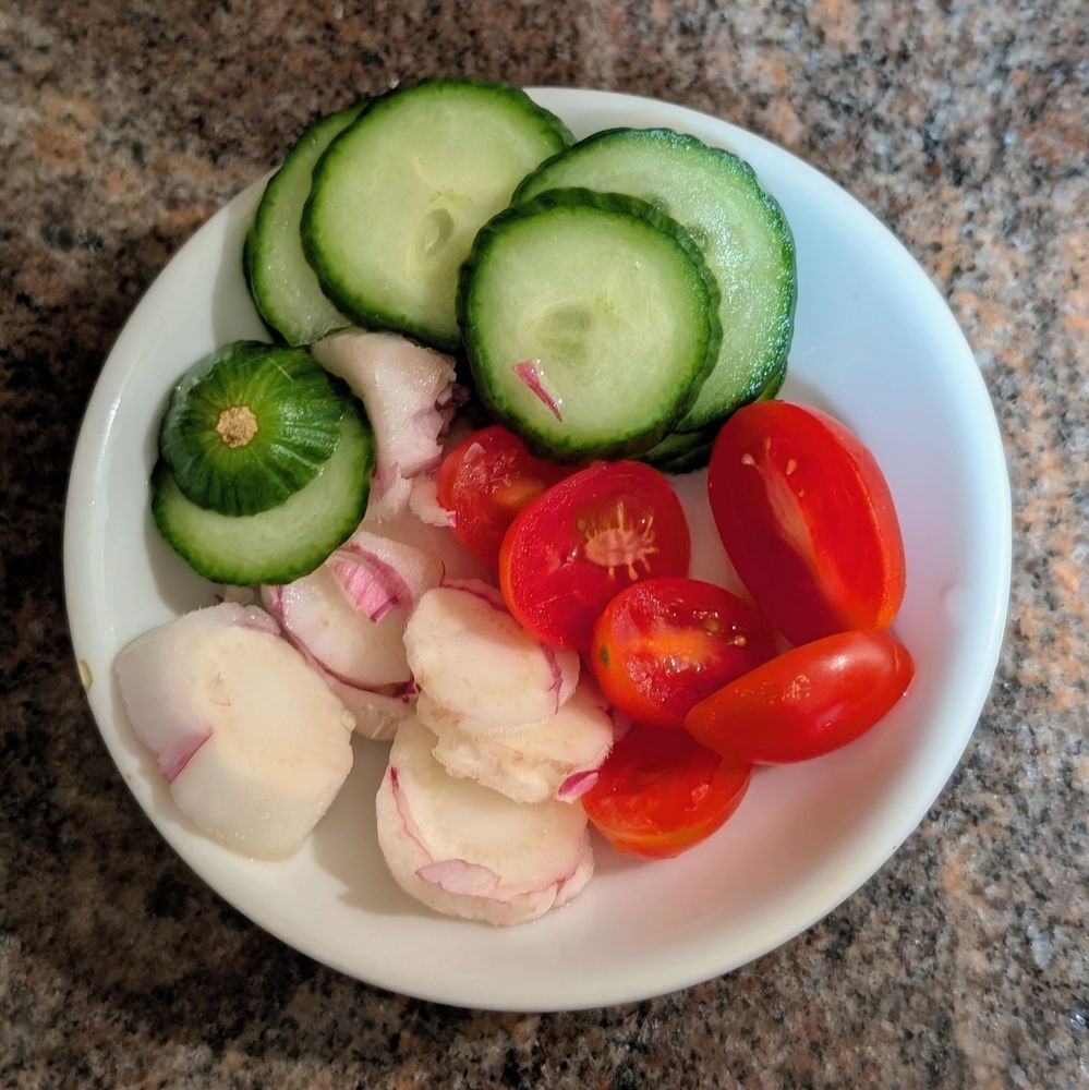 Cucumber, sliced endive, and tomatoes on a small white dish 