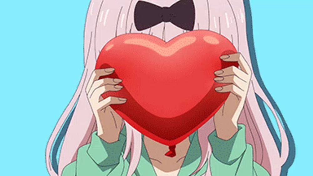 a girl is covering her face with a heart shaped object .