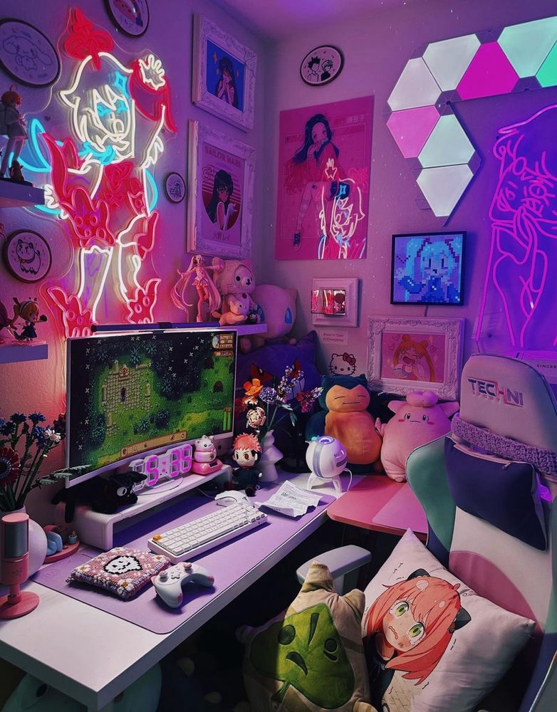 A cozy, pastel-themed gaming setup with vibrant neon lights illuminating the space. A dual-monitor desk setup features a mechanical keyboard, a pink gaming mouse, and a decorated desk mat with cute designs. Surrounding the desk are plushies, anime-themed pillows, and a mix of framed artwork and neon wall art, including glowing outlines of characters. Hexagonal RGB wall panels add a futuristic touch, while the space is filled with whimsical details that create a playful and creative atmosphere.