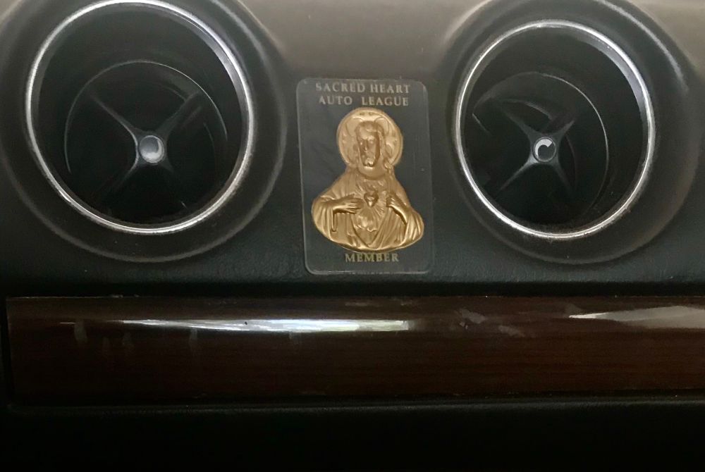 A gold icon of the Sacred Heart of Jesus between the vents in a 1982 Mercedes 300D