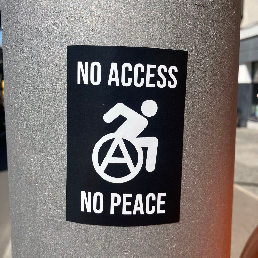 Ein Pic, Programm von einem Menschen in einem Rollstuhl, anstatt eines Reifens ein großes A in einem Kreis. Dazu der Text:

NO ACCESS
NO PEACE