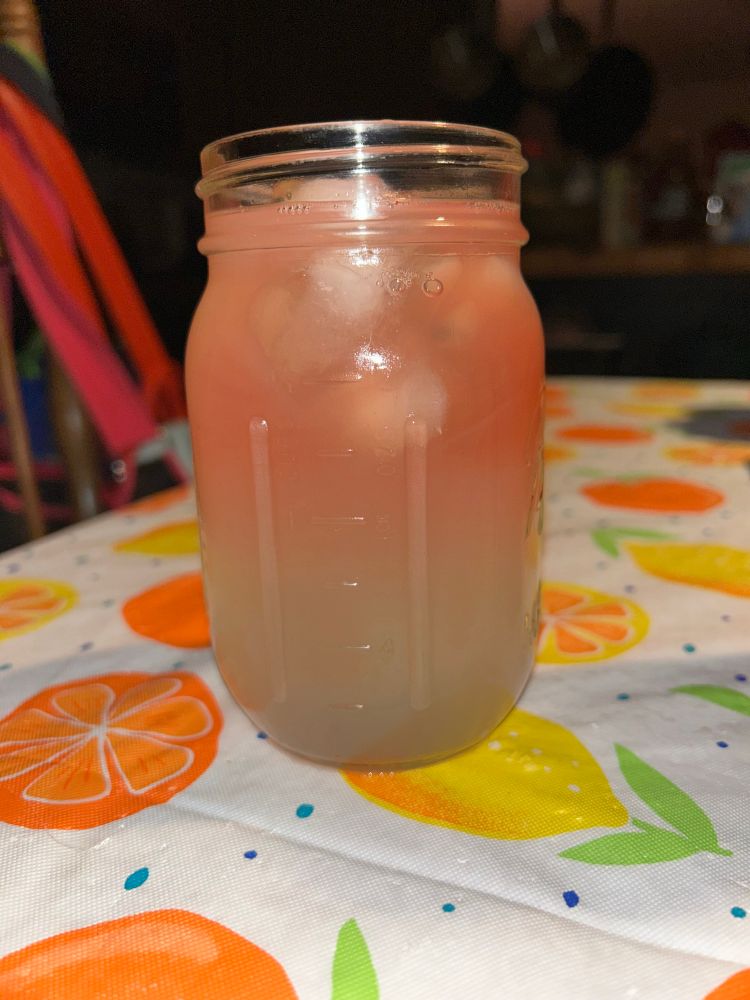 a mason jar sits on a table with a white tablecloth covered in oranges and lemons. the jar is full of lemonade with fresh watermelon juice