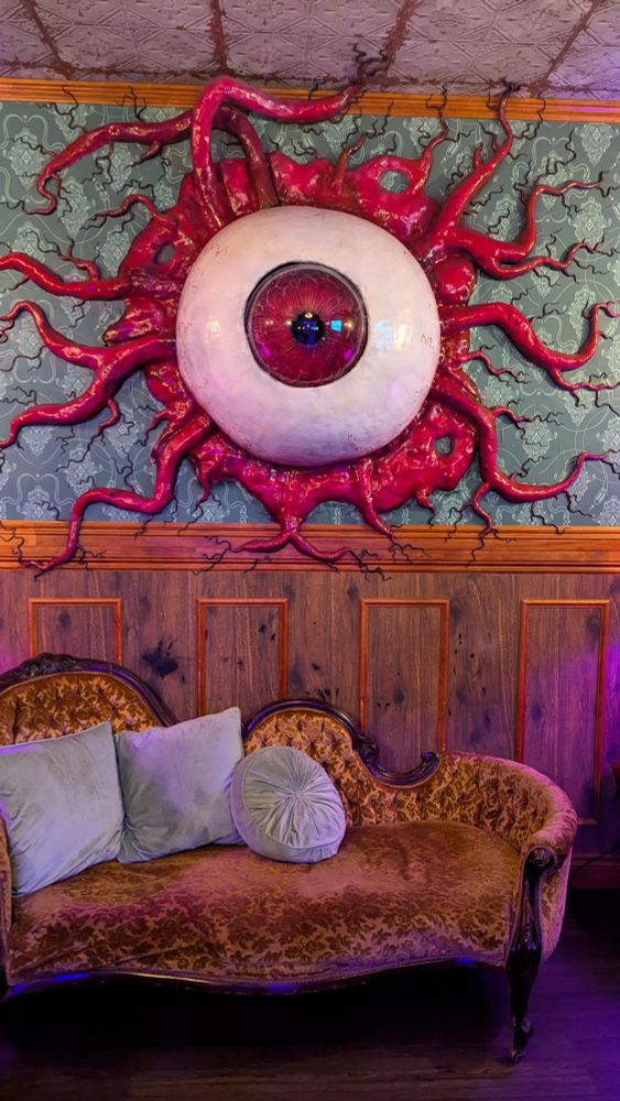 A room built to look like a fancy, old timey lounge room with a huge monster eye sticking through the wall.