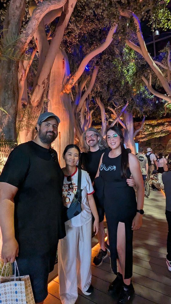Portrait photo of four friends standing in front of fake eucalyptus trees in an exhibit of the Australian bush.
