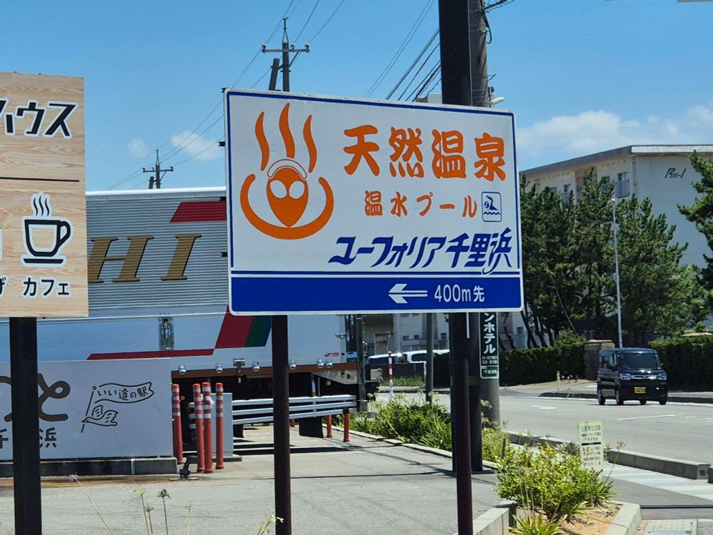A street sign in Japanese which I can't meaningfully translate for alt text BUT the icon is the Hot Spring icon with an Alien in it.