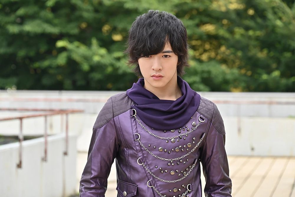 A picture of Chase from Kamen Rider Drive. He's wearing his typical outfit of a purple jacket with chains running across the front, complimented by a scarf with a darker shade of purple.