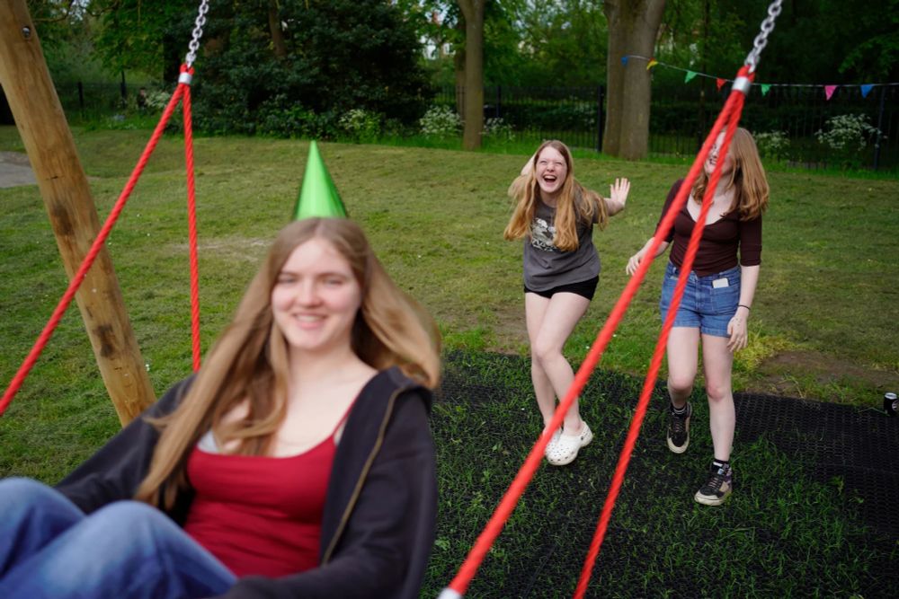 Two teenage girls push another one on a big swing, they all look very happy