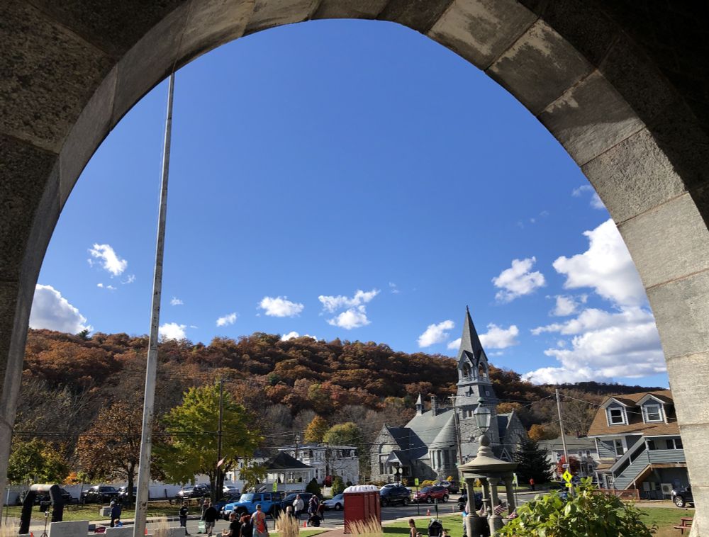 View from the arched-over stairs into the hall, looking out across the lawn to the street, to an ornate steepled church and some town buildings with a steep wooded hill right behind (Monson is generally pretty hilly!). Took this after I'd finished, but people are still coming in to the finish arch visible at lower left.
