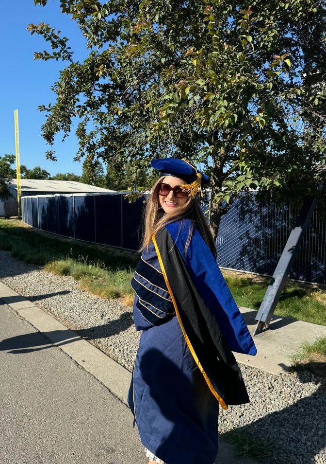 Anna turning to look at the camera wearing UC Davis doctoral regalia and sunglasses