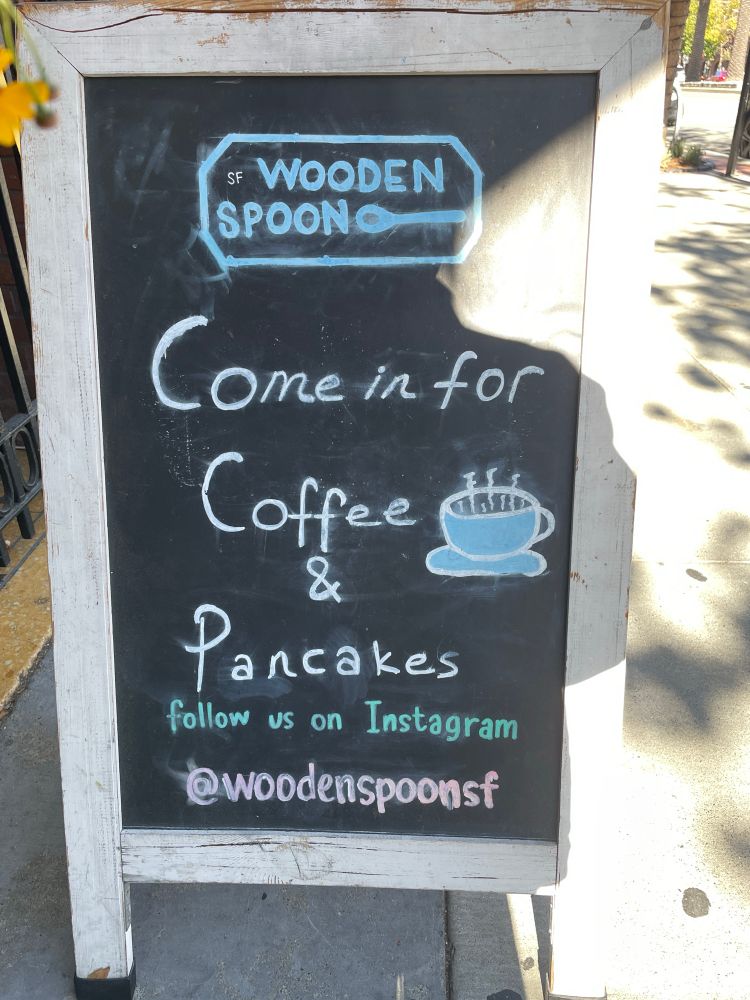 Slate sandwich board outside a restaurant with hand-lettered “come in for coffee & pancakes” written in chalk 