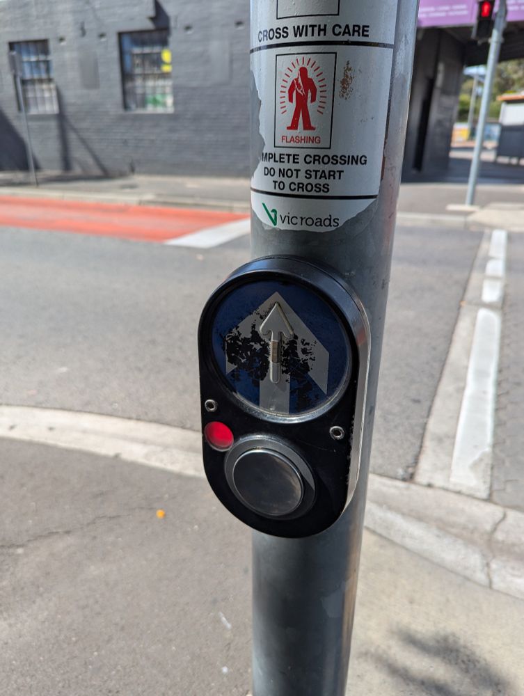photo of a slightly worn PB5 pedestrian crossing button with the light indicating that it has been pressed illuminated 