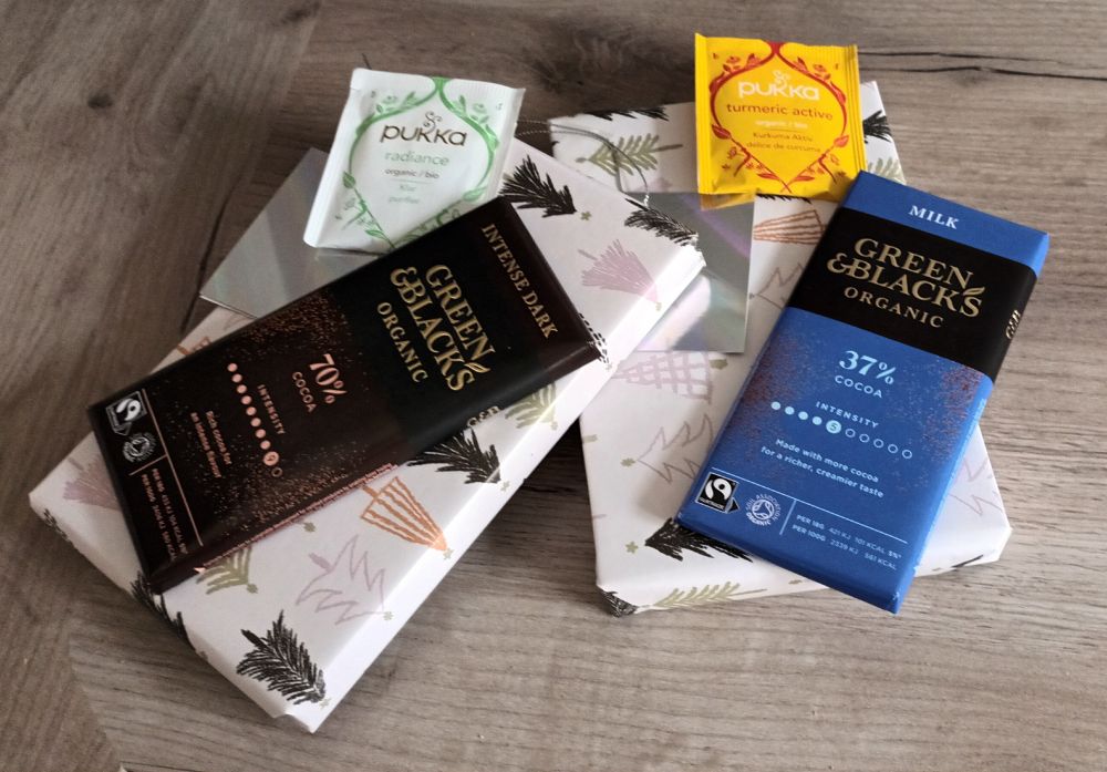 Two books, wrapped in festive paper, with a bar of chocolate and a packet of tea on each of them. 