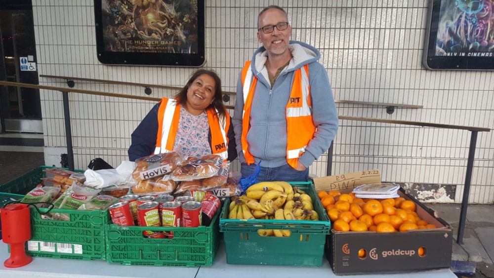 two people standing behind a table with crates of fresh food on it. 