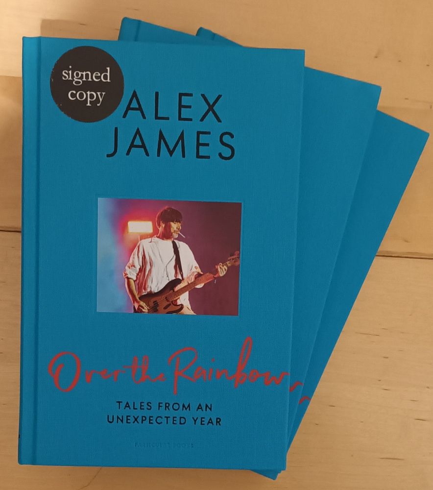 The front cover of Alex James new book. It's has a blue surrounding and in the middle is a photo of "classic" Alex. He's got a fag in has mouth and he's smashing it on the bass. 
