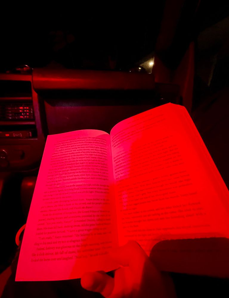 A photograph of a book sitting on someone’s lap. The reading light is red.
